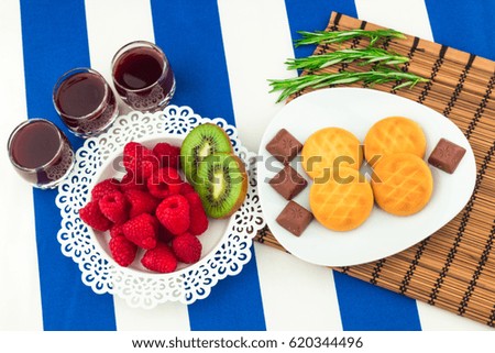 Fresh Red Raspberries on a white artistic plate / Red Fresh Raspberries on a white artistic plate with cookies, rosemary, chocolate and cream in the background.