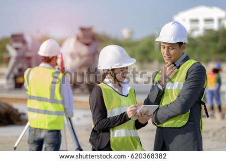 Civil Engineers At Construction Site in discussion and A land surveyor using an altometer in background