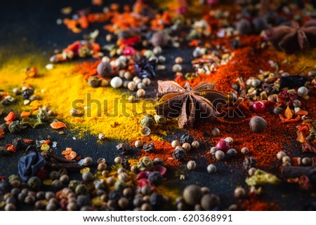 Different varicolored seasonings (coriander, a mixture of peppers peas, turmeric, sweet red pepper powder, anise) on a black background chalkboard,