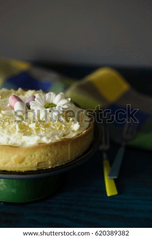 Lemon tart with whipped cream, decorated with chocolate eggs and a flower. Dark, moody, low key lighting, creamy bokeh.