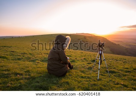Photographer taking photos from a hill at sunset. Camera on a tripod