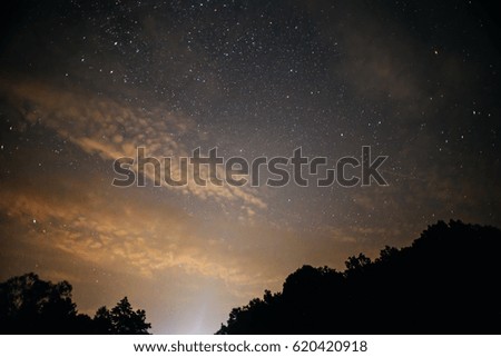 A clear night sky with a hill and trees in the foreground.