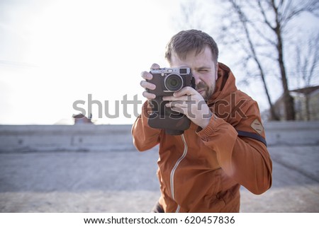 Serious travel photographer with the camera on a sunny day on the background of a concrete wall and wooden houses.
