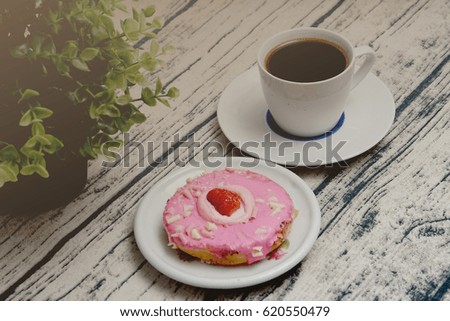 Pink strawberry doughnuts and cup of coffee for afternoon break. Vintage editing and selective focus.