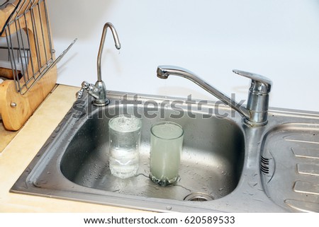 Filling a glass of clean and muddy water from a filter and a kitchen faucet
