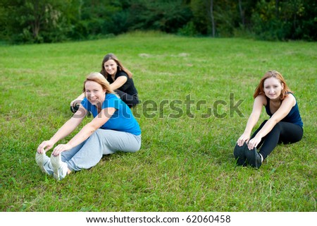 Workout - Group of three cute activ girls workout outdoor on a grass field near brink of a forest