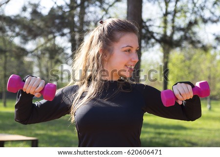 Beautiful young woman doing exercise with weights in the park. Selective focus and small depth of field.