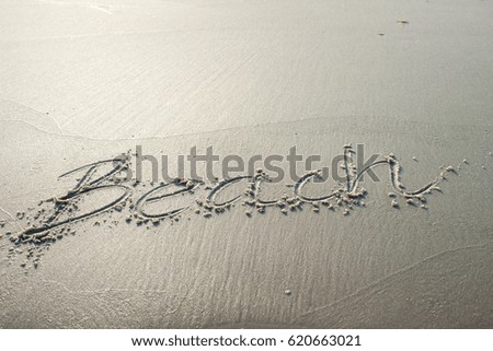 The word beach hand drawn in sand on isolated deserted beach by ocean shore at sunset on a calm and peaceful beautiful evening; vacation background with sandy copy space