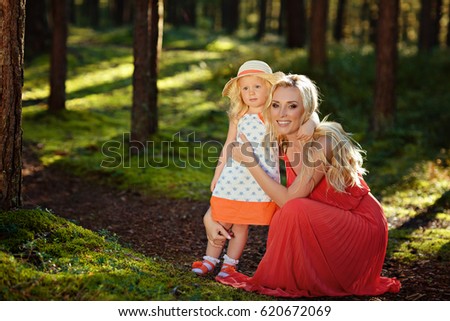 Little blonde girl and her mom smiling in the forest in sunny summer.