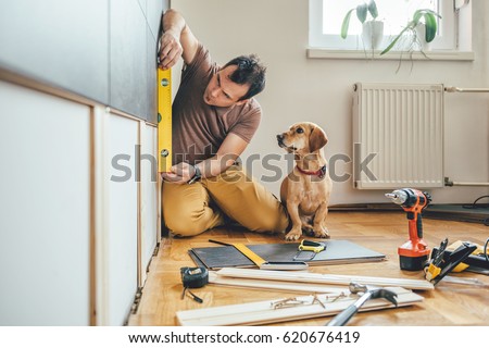 Man doing renovation work at home together with his small yellow dog Royalty-Free Stock Photo #620676419