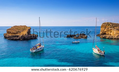 Comino, Malta - Sailing boats at the beautiful Blue Lagoon at Comino Island with turquoise clear sea water, blue sky and rocks in the water Royalty-Free Stock Photo #620676929