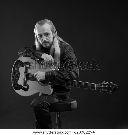 Black and white portrait of a elderly gray-haired male musician with long hair with a guitar in his hands playing and posing on a black background