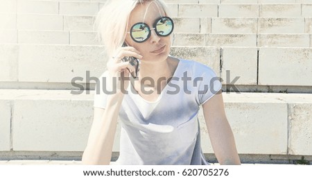 Blonde caucasian young woman wearing fashionable sunglasses, talking by mobile phone.