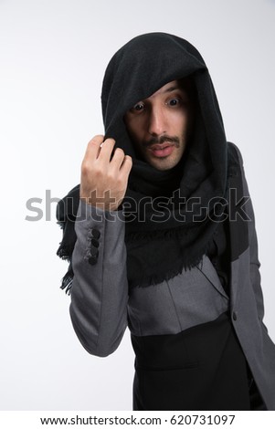 The guy from Syria looks down. Holds a scarf with his right hand. In a black and gray suit. On a gray background. The look of a surprised man .