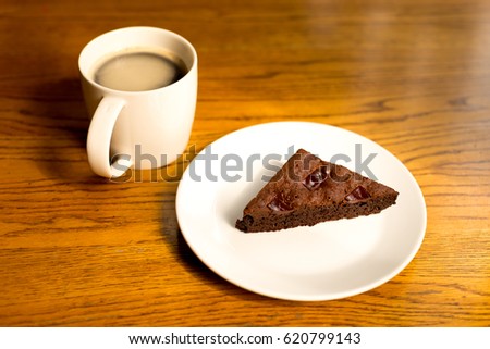 Brownie on a plate with  a cup of coffee on the wooden table