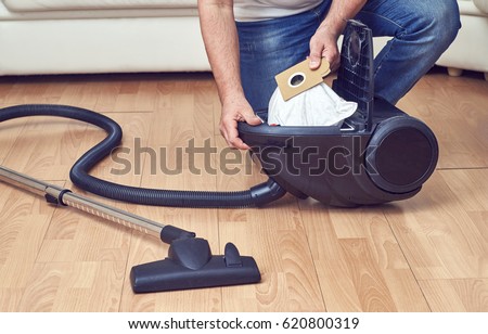 Man taking out a full dust bag from a vacuum cleaner                                Royalty-Free Stock Photo #620800319
