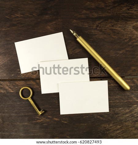 An overhead photo of blank white thick cardboard business cards on a dark wooden background texture with a golden ink pen and a vintage key. A square mockup or a minimalist banner with copy space