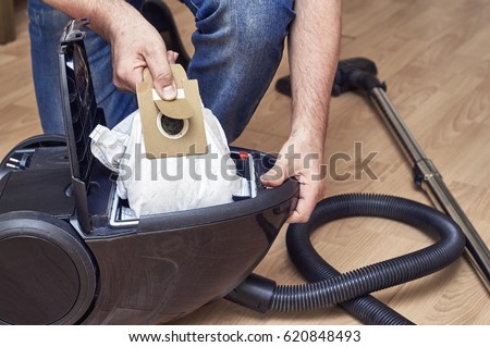 Man replaces a dust bag in a vacuum cleaner                               Royalty-Free Stock Photo #620848493