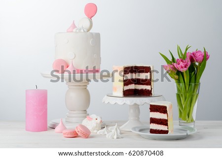 Tulips, a cake on the ceramic cake stand, macaroni sweets, a ceramic bunny and a Red Velvet cake, close-up. Light wooden surface, neutral background. Spring mood.