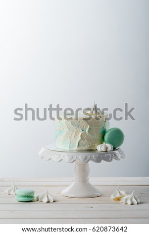 Exquisite cake on a stand, meringues and bright macaroni sweets on the light grey background. Wooden surface, place to insert your text. Happy Birthday.