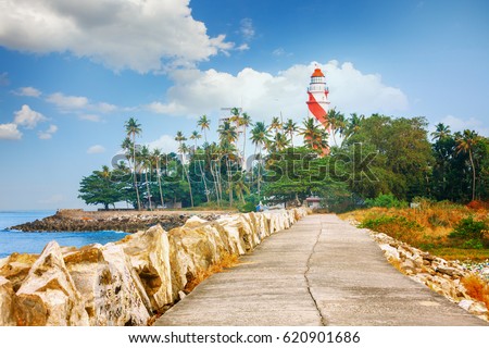Thangassery red and white stripe Lighthouse on the cliff Quay breakwater surrounded by palm trees and big sea waves on the Kollam beach. Kerala, India Royalty-Free Stock Photo #620901686