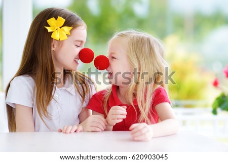Happy little sisters wearing red clown noses having fun together on sunny summer day at home. Two kid playing together. Royalty-Free Stock Photo #620903045