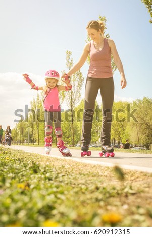 Smiling mother assisting her little girl in rollerblading.