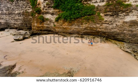 Two young men stand on the sand at the rock on an inhabited island. Aerial view.