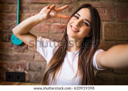 Beautiful stylish girl making selfie with victory gesture