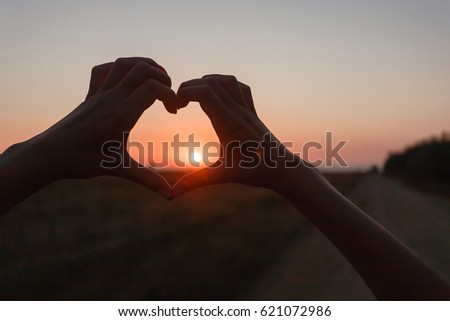 Young girl holding hands in heart shape framing setting sun a beautifult sunset on beach. 