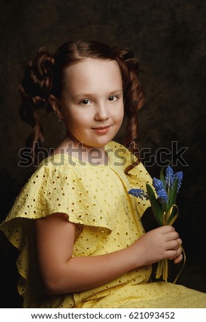 portrait of a little girl in a yellow dress with blue flowers in her hands in Studio on dark background