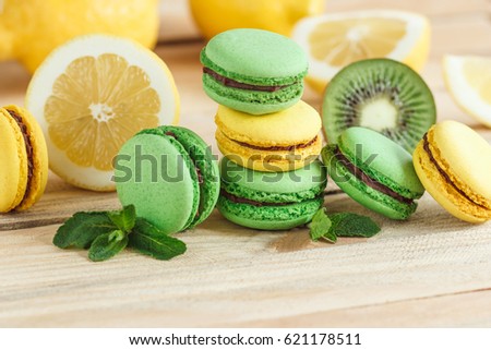 Green and yellow french macarons with kiwi, lemon and mint decorations, soft focus background