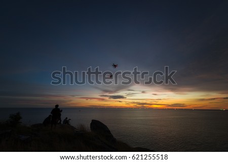 Silhouette of a man photographer is using RC aerial drone for video shooting while is standing on mountain from the view point Phuket southern of Thailand at Beautiful sunset time