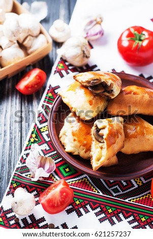 Hearty and tasty food, national Ukrainian cuisine, pies made of yeast dough with mushrooms, tomatoes and spices on rushnyk on a dark rustic wooden background  