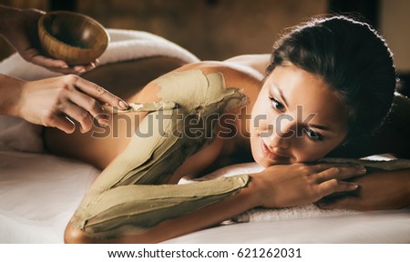 The girl enjoys mud body mask in a spa salon. Focus on the hand with the stick. Luxury treatment. Royalty-Free Stock Photo #621262031