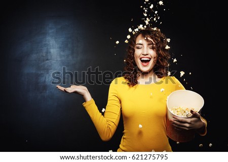 Smiling young woman staying under popcorn shower with right hand up