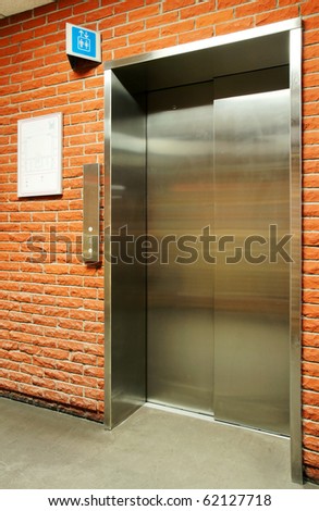 Vertical of closed steel door elevator in orange brick wall with blue sign.