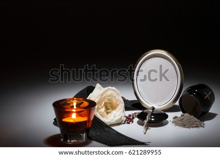 black urn with black tape,white rose,candle, rosary for sympathy card on dark background