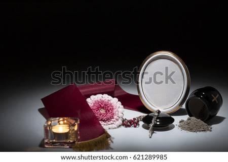 black urn with red tape, gerbera flower, candle, rosary for sympathy card on dark background