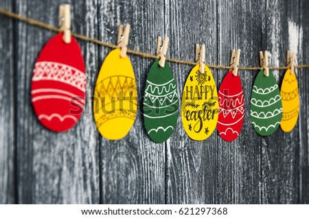 Side view. Easter day background. April 17. Painted greeting cards in the shape of eggs with massage "Happy Easter" on clothespins On the wooden table background. Copy Space for your text
