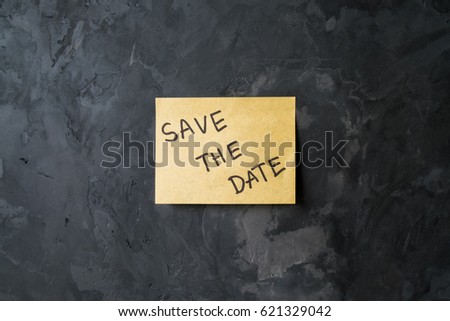 message "save the date" on sticky note paper on cement wall texture background, loft style
