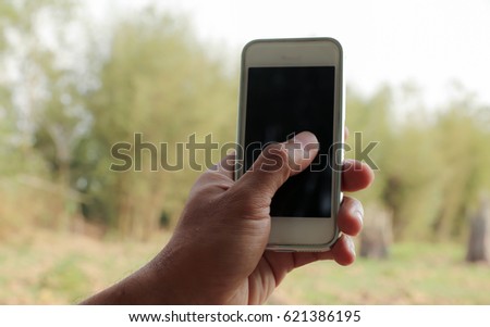 Hand holding smart phone with blank screen against spring green nature background.