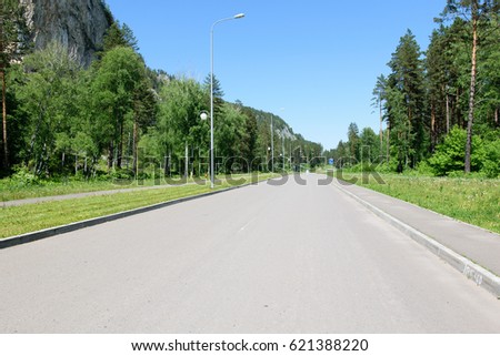 Asphalt road with sidewalks and streetlights on a sunny summer day in the forest. In Altai region.