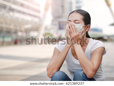 Woman wearing protective mask to protect pollution and the flu sitting at public area. Royalty-Free Stock Photo #621389237