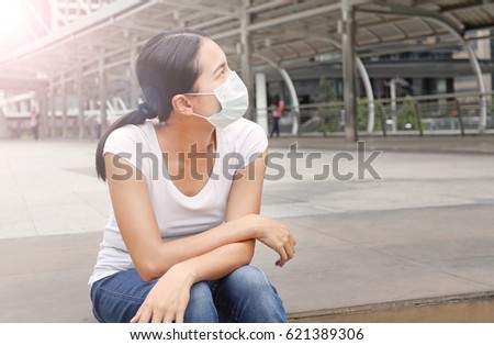 Woman wearing protective mask to protect pollution and the flu sitting at public area.