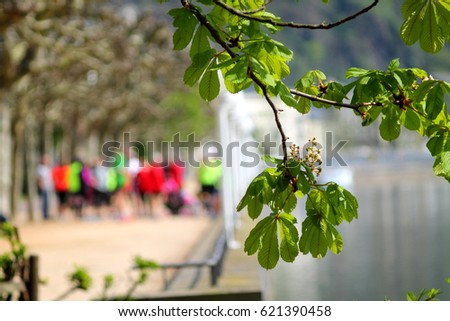 Blurred bright figures on river embankment. Soft horse chestnut branches with first green leaves frames the picture.