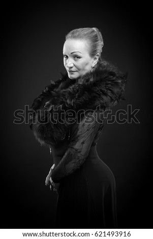 Black and white portrait of a beautiful mature woman in a theatrical costume with boa posing on a black background