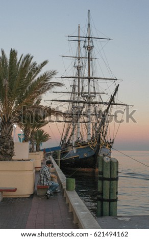 Tall ship graces a palm lined sidewalk at sunset at Florida pier.