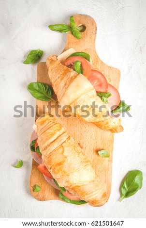 Light and hearty spring breakfast. Croissant with ham, cheese, fresh tomatoes and basil. On a white stone table, with the ingredients. Copy space top view 