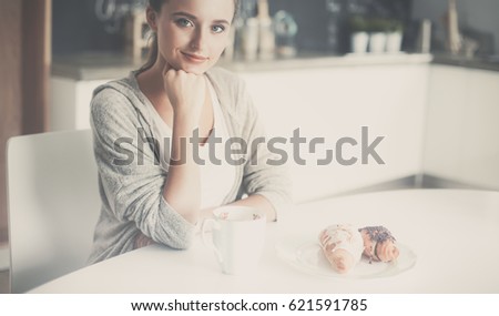 Woman drinking tea with sweet croissant at the kitchen table